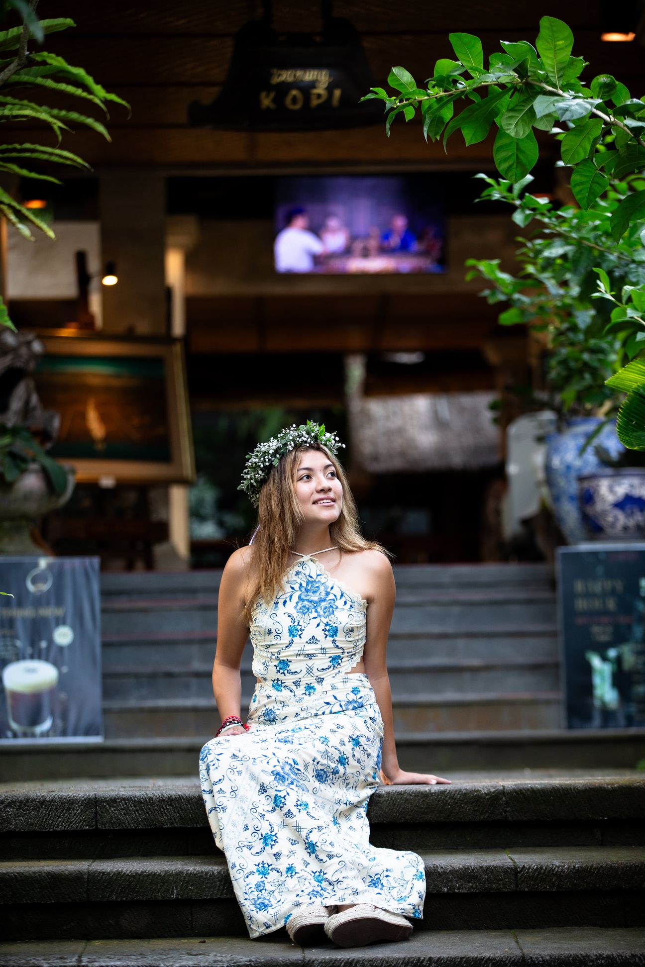 A woman in a floral dress poses in the shade of a tropical Balinese garden