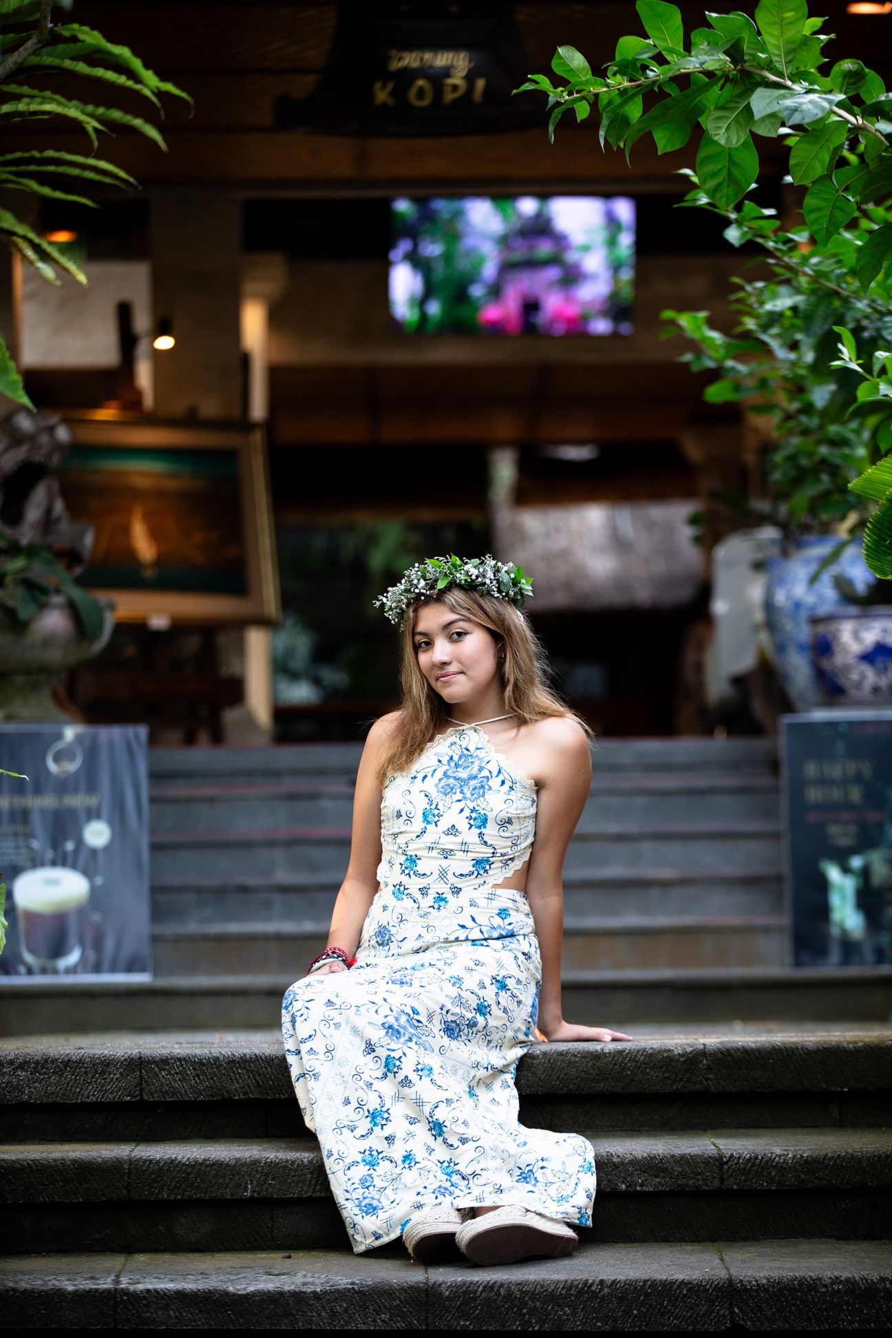 A woman in a floral dress poses in the shade of a tropical Balinese garden