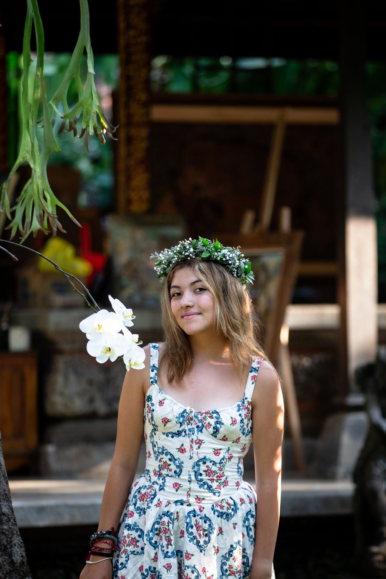 A woman in a floral dress poses in the shade of a tropical Balinese garden