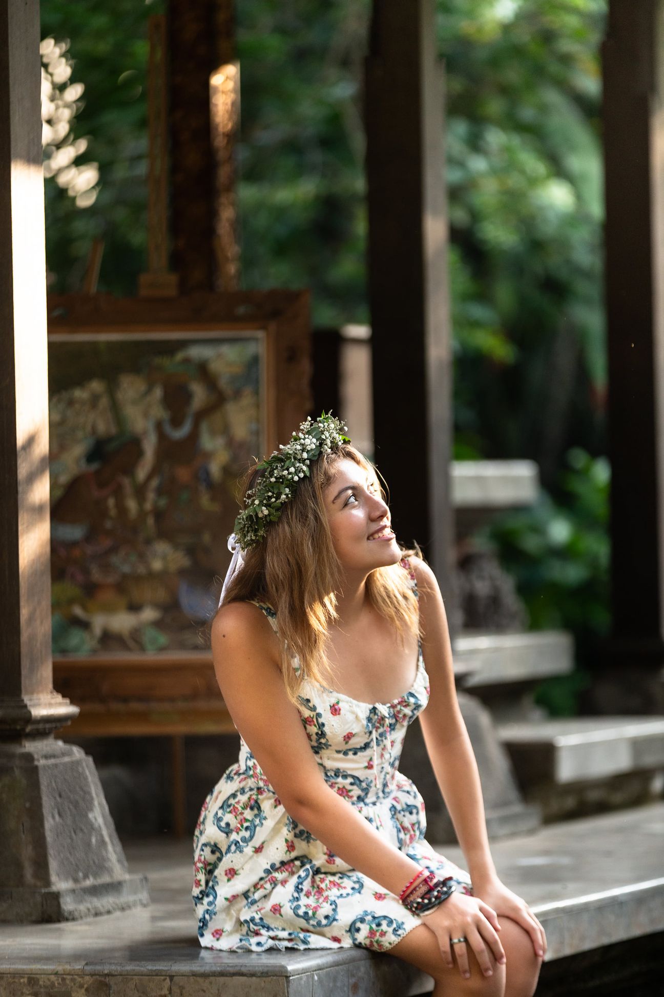 A woman in a floral dress poses in the shade of a tropical Balinese garden