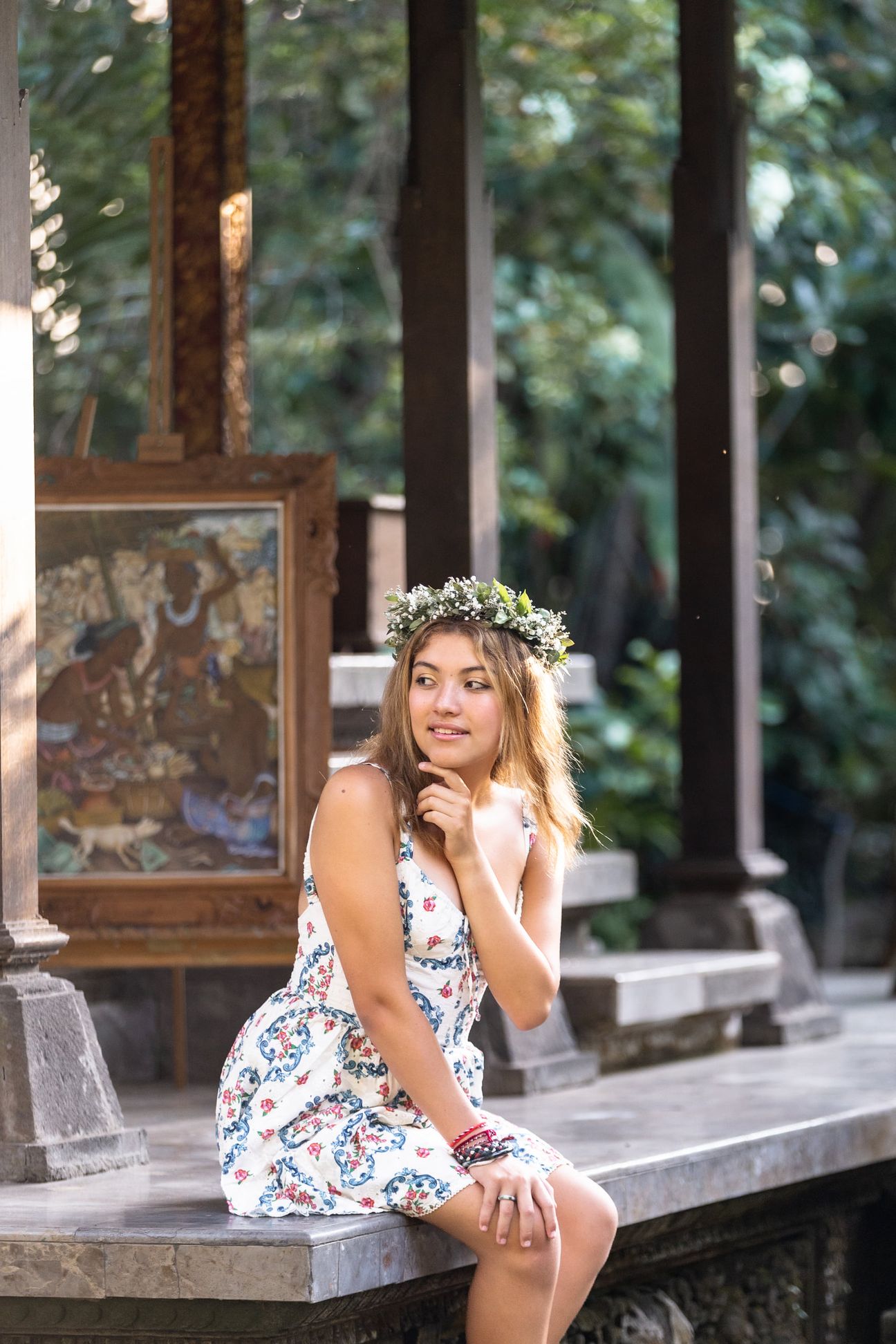 A woman in a floral dress poses in the shade of a tropical Balinese garden