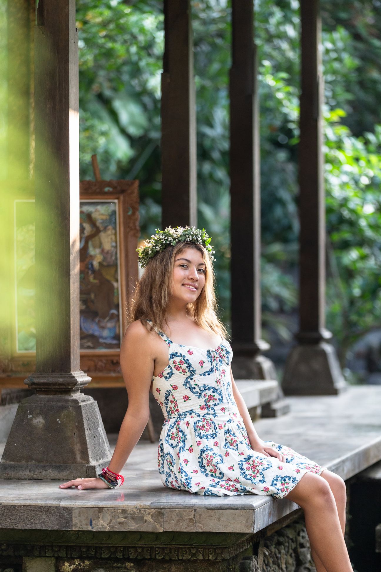 A woman in a floral dress poses in the shade of a tropical Balinese garden