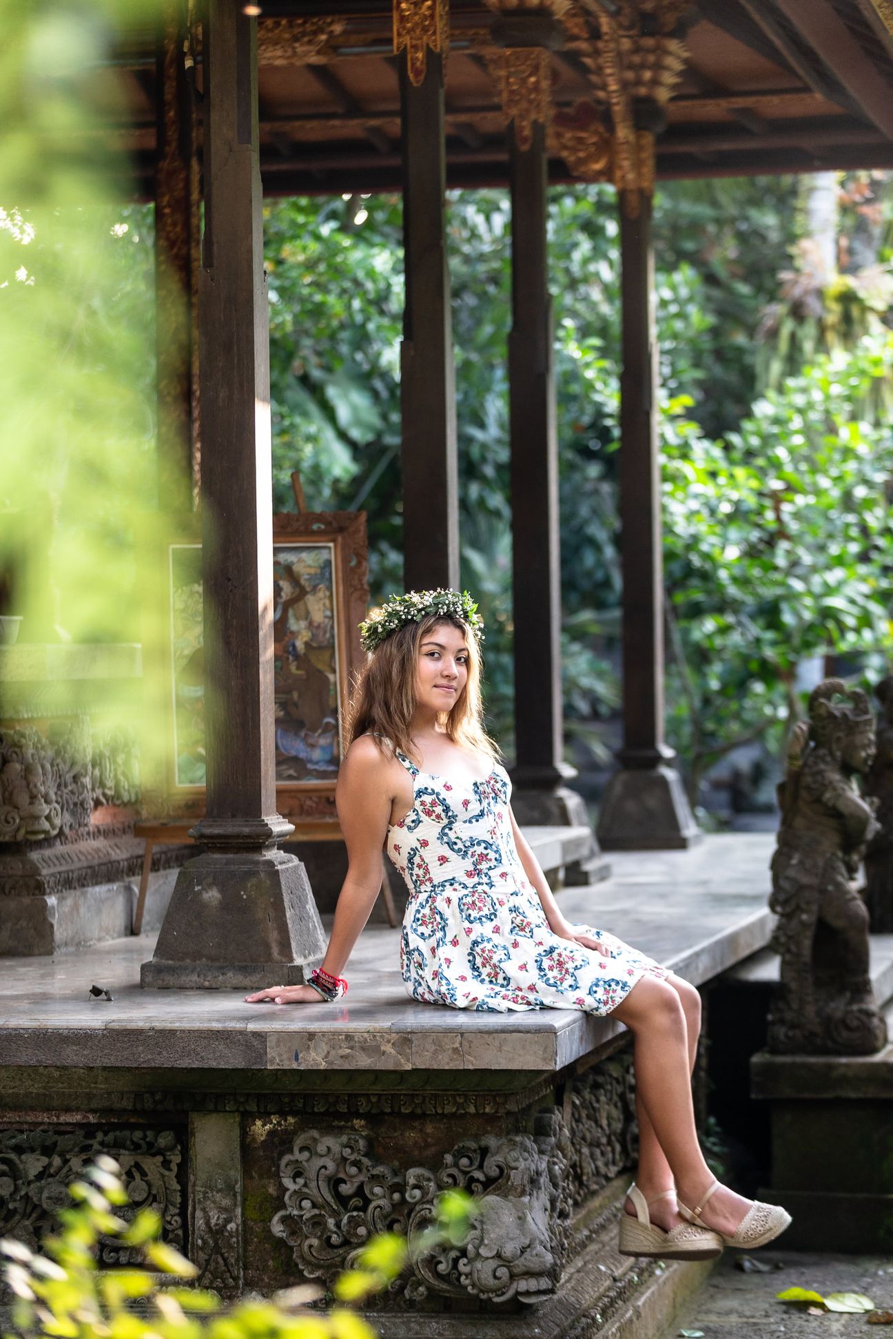 A woman in a floral dress poses in the shade of a tropical Balinese garden