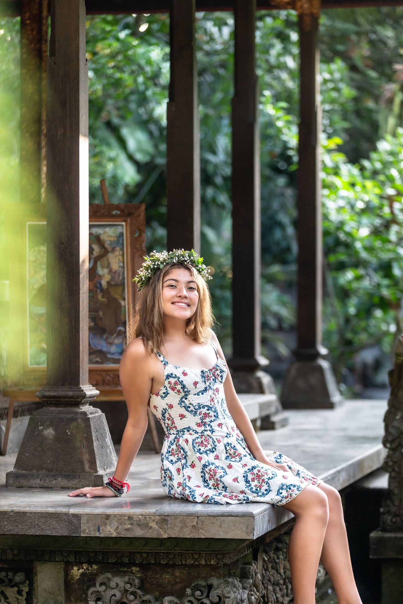 A woman in a floral dress poses in the shade of a tropical Balinese garden