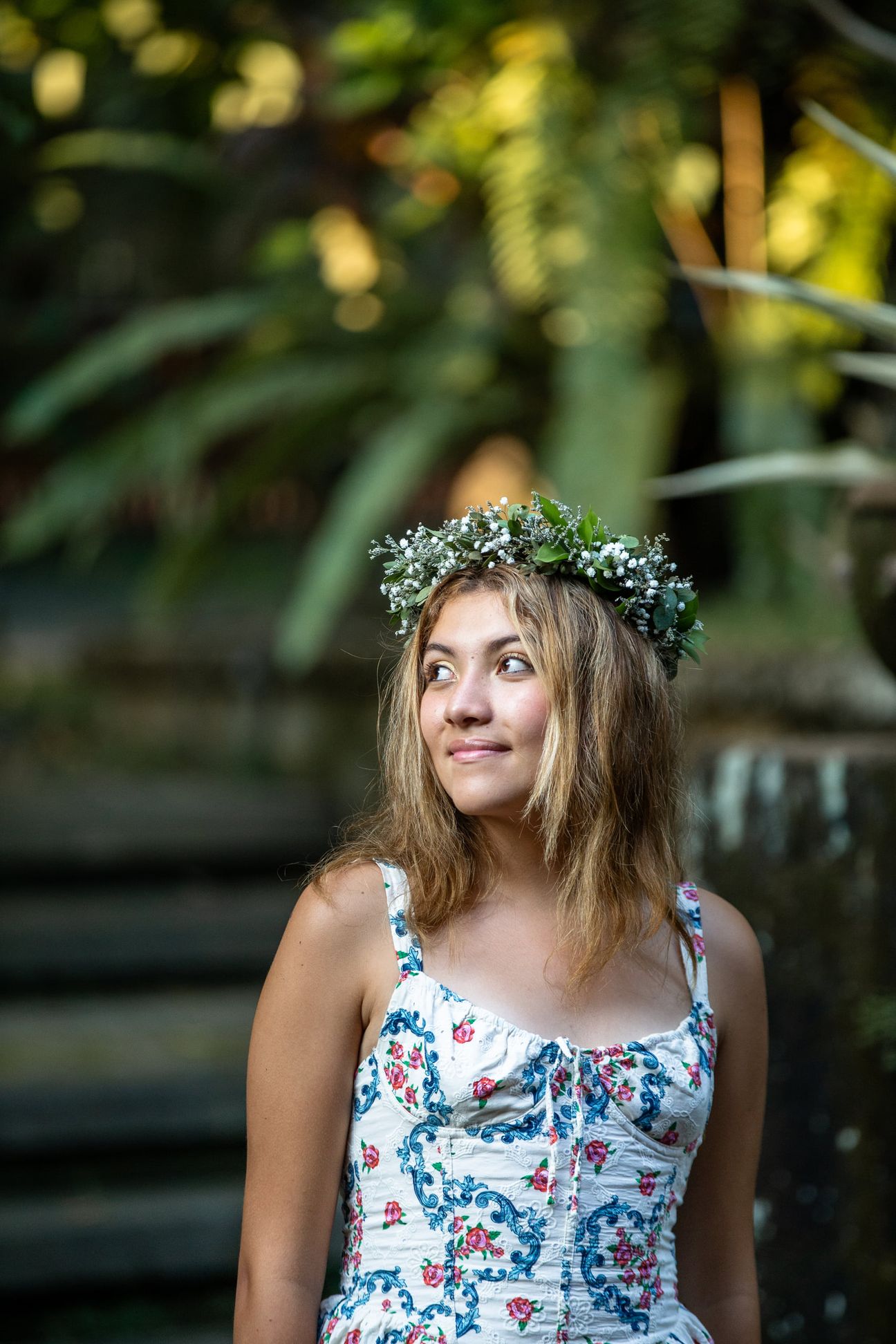 A woman in a floral dress poses in the shade of a tropical Balinese garden