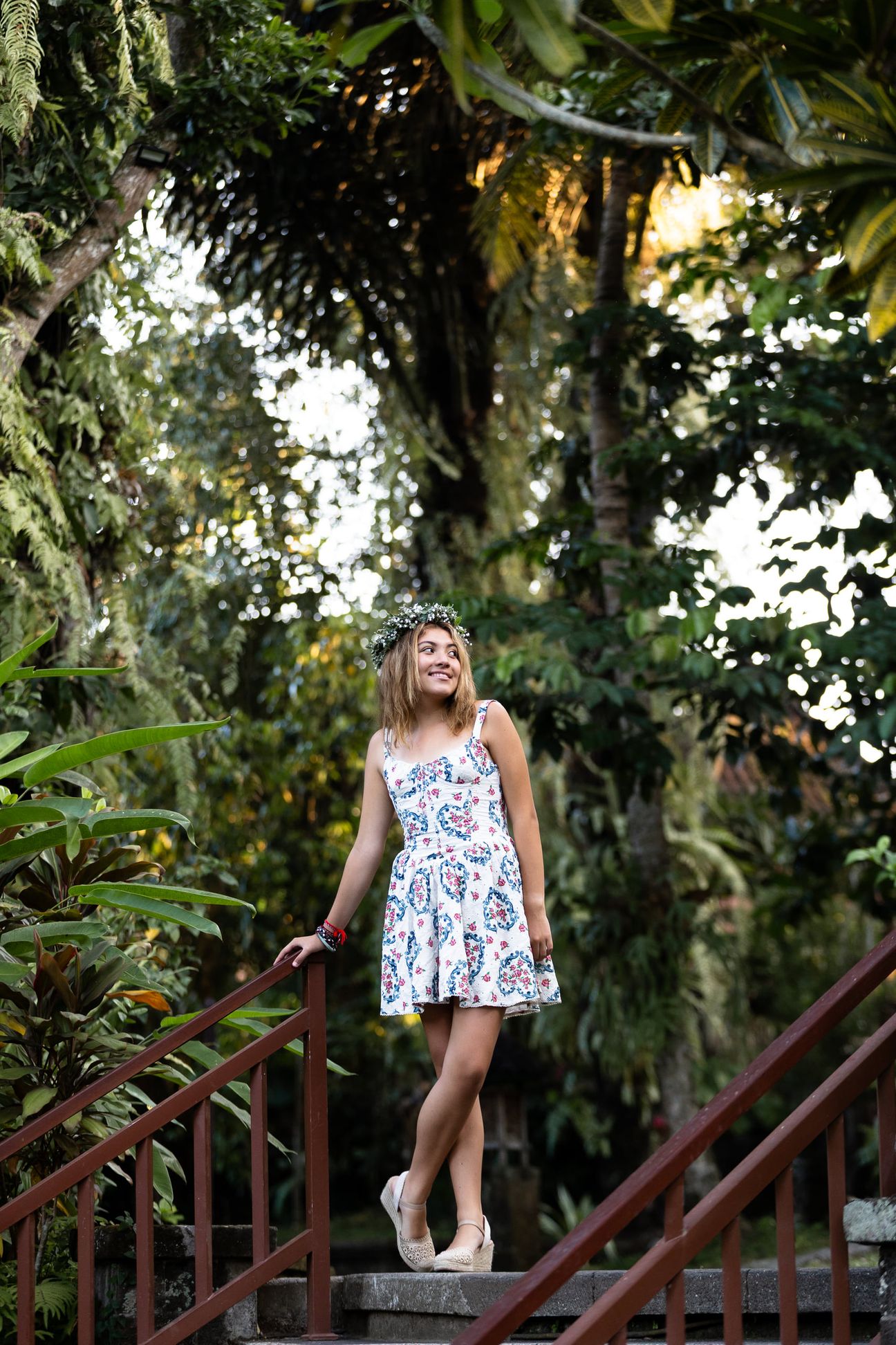 A woman in a floral dress poses in the shade of a tropical Balinese garden