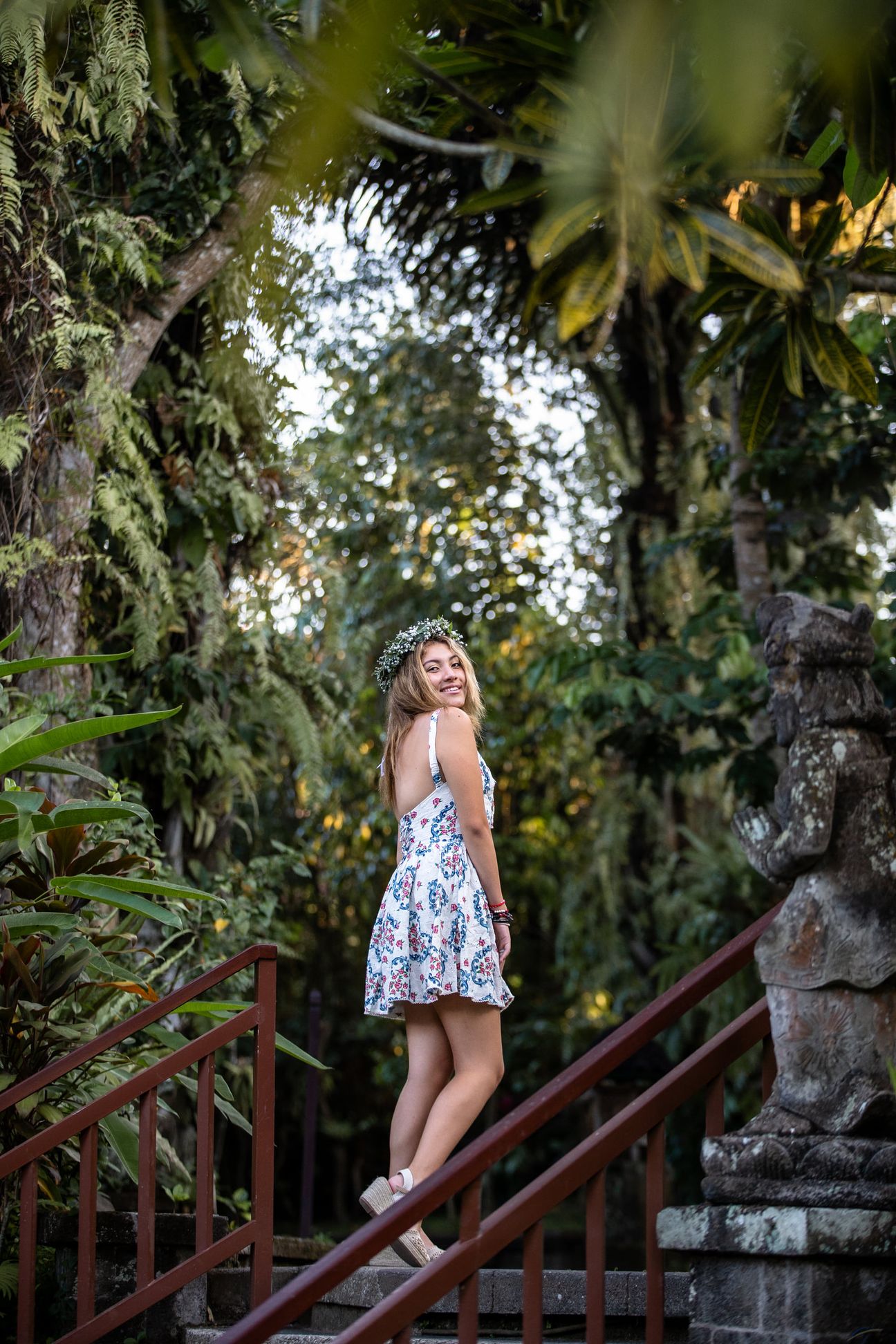 A woman in a floral dress poses in the shade of a tropical Balinese garden