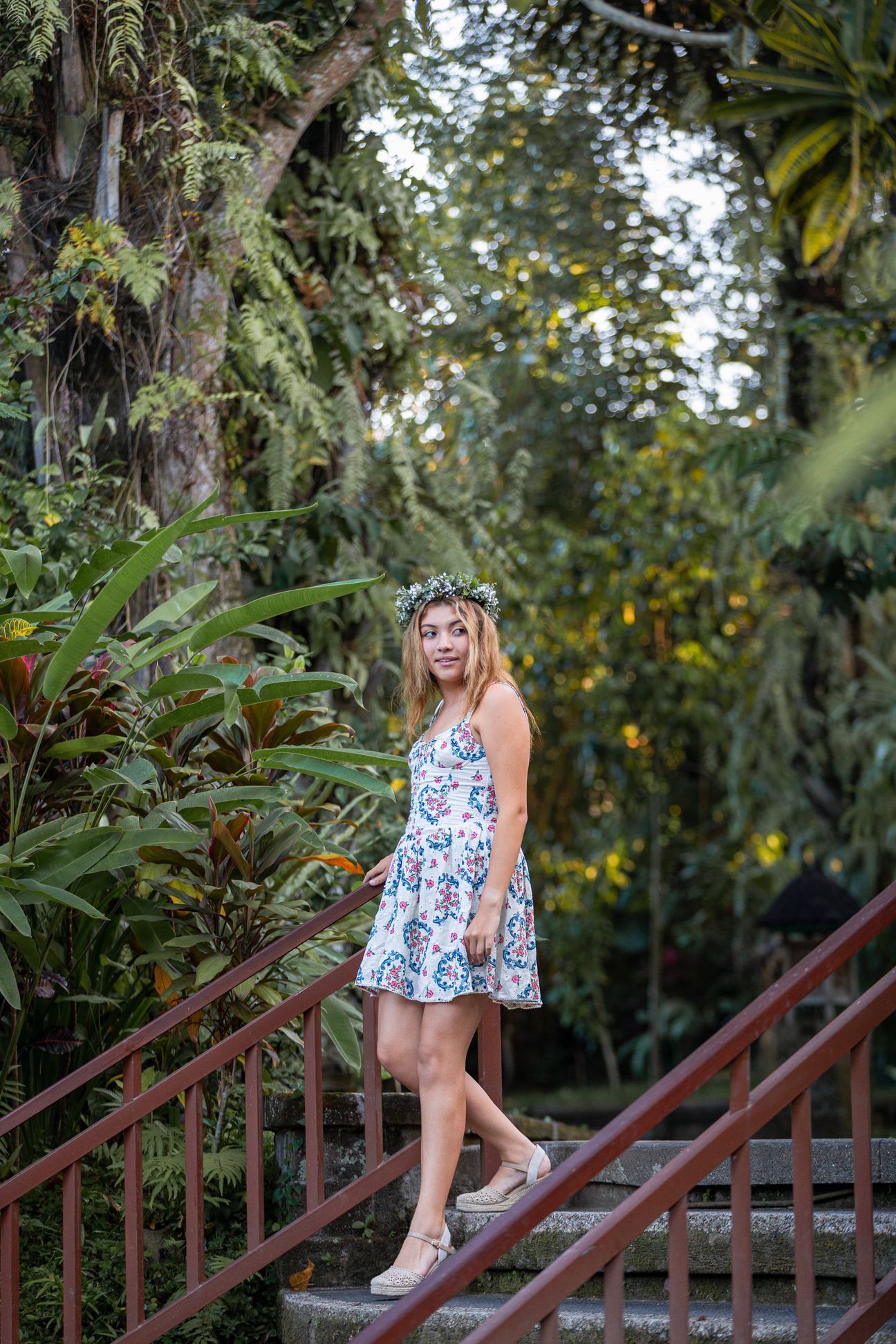 A woman in a floral dress poses in the shade of a tropical Balinese garden
