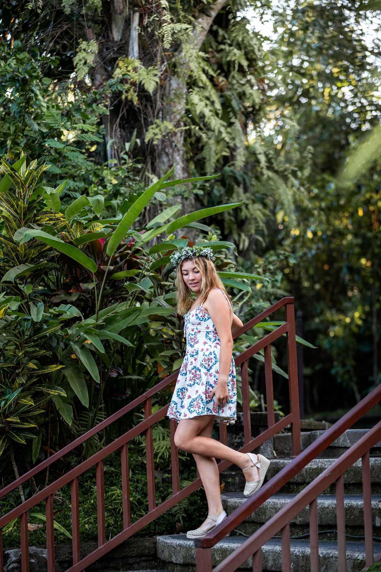 A woman in a floral dress poses in the shade of a tropical Balinese garden