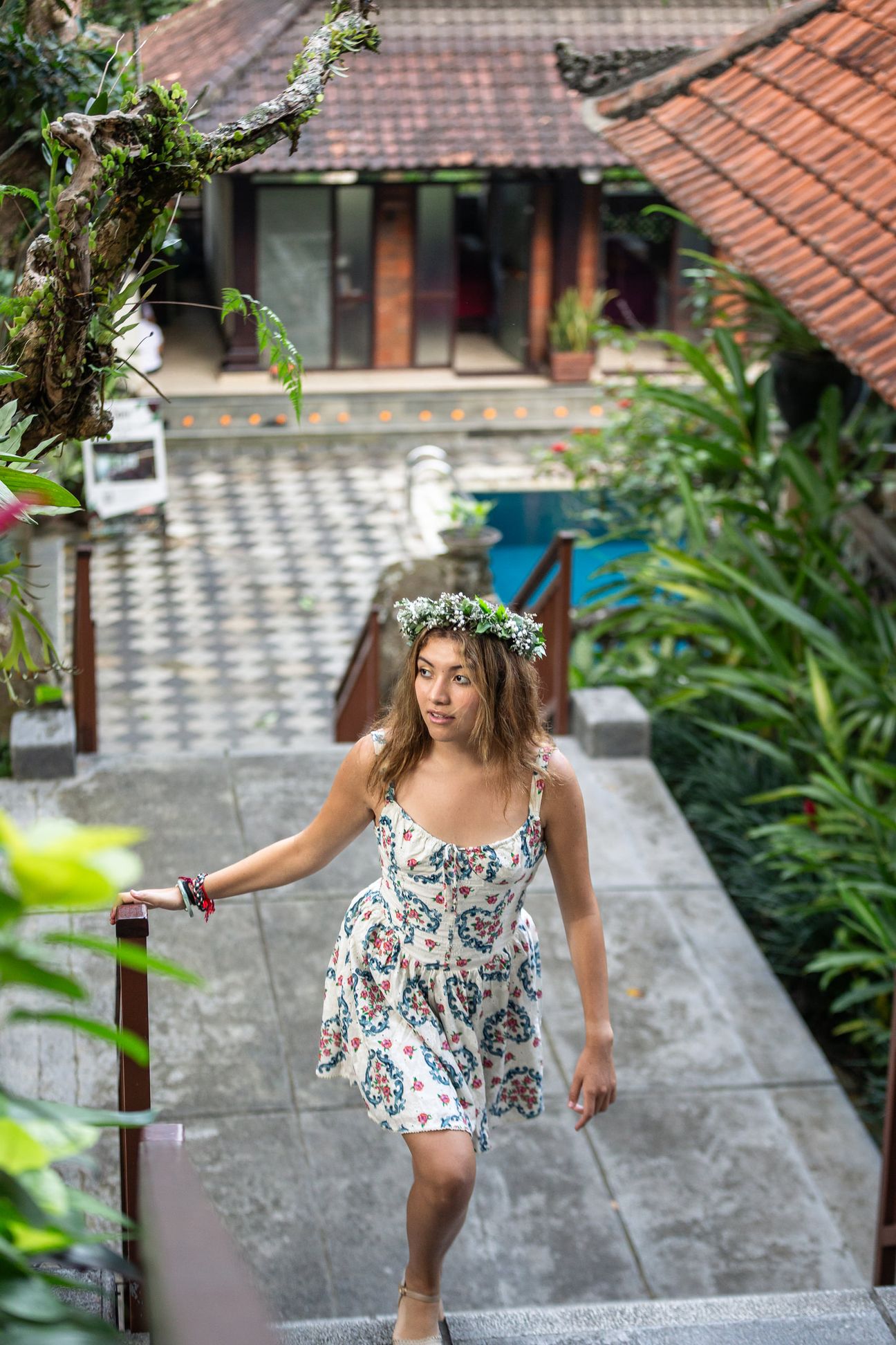 A woman in a floral dress poses in the shade of a tropical Balinese garden
