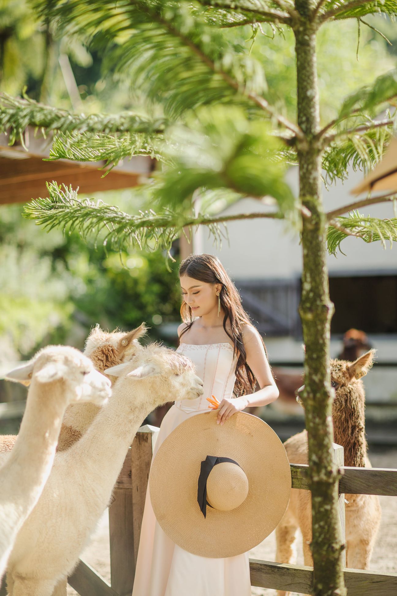 A woman in a white dress stands beside deer beneath tall trees