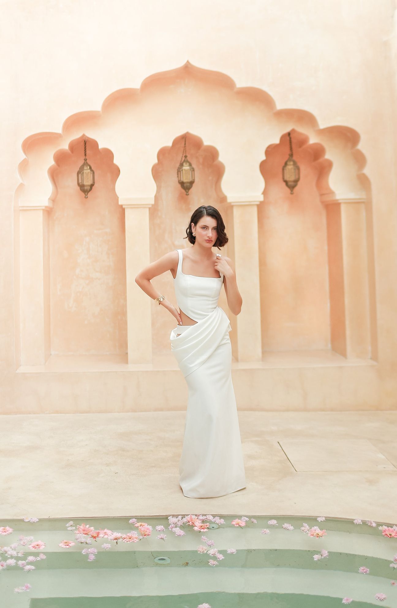 A woman in a white dress poses beneath warm sculpted arches