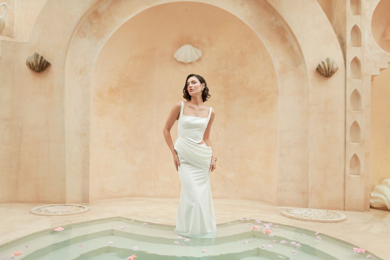 A woman in a white dress poses beneath warm sculpted arches