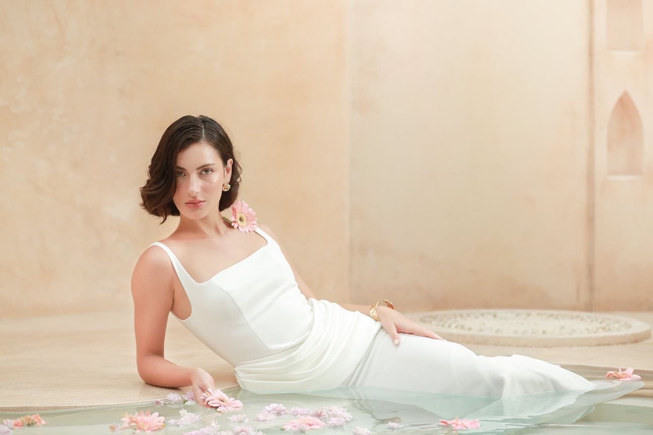 A woman in a white dress poses beside pale stone and still water