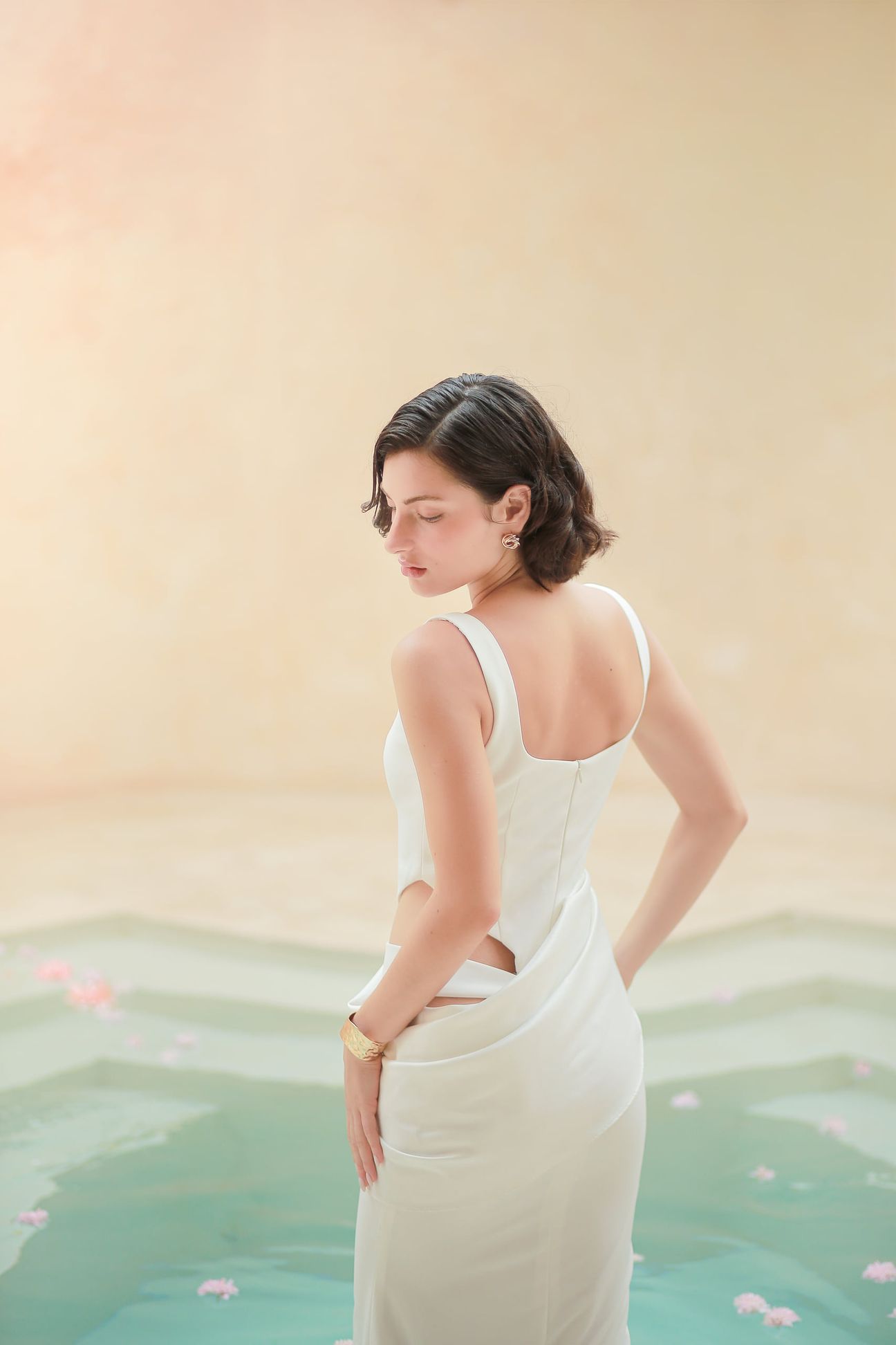 A woman in a white dress poses beside pale stone and still water