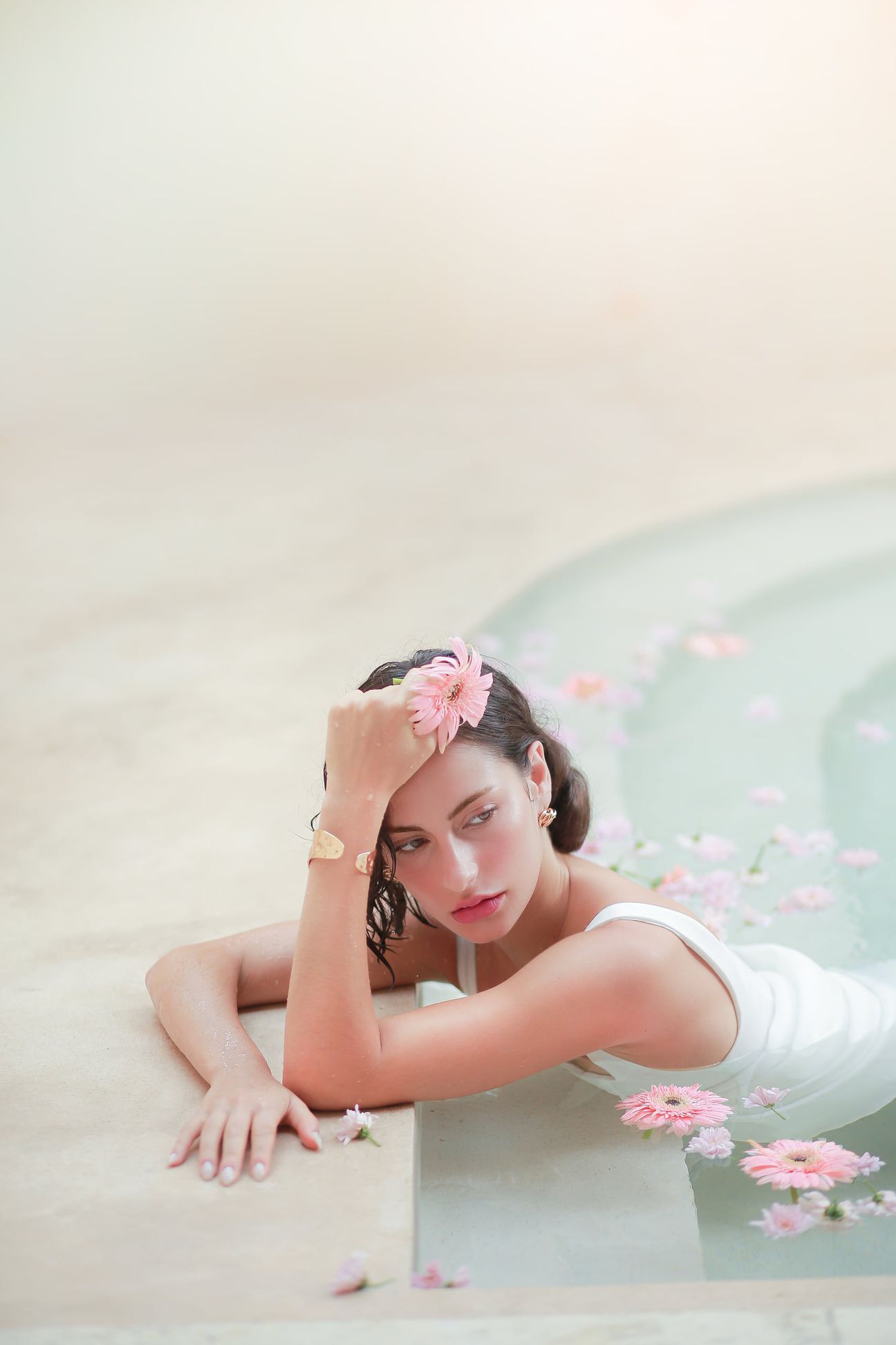 A woman in a white dress poses beside pale stone and still water