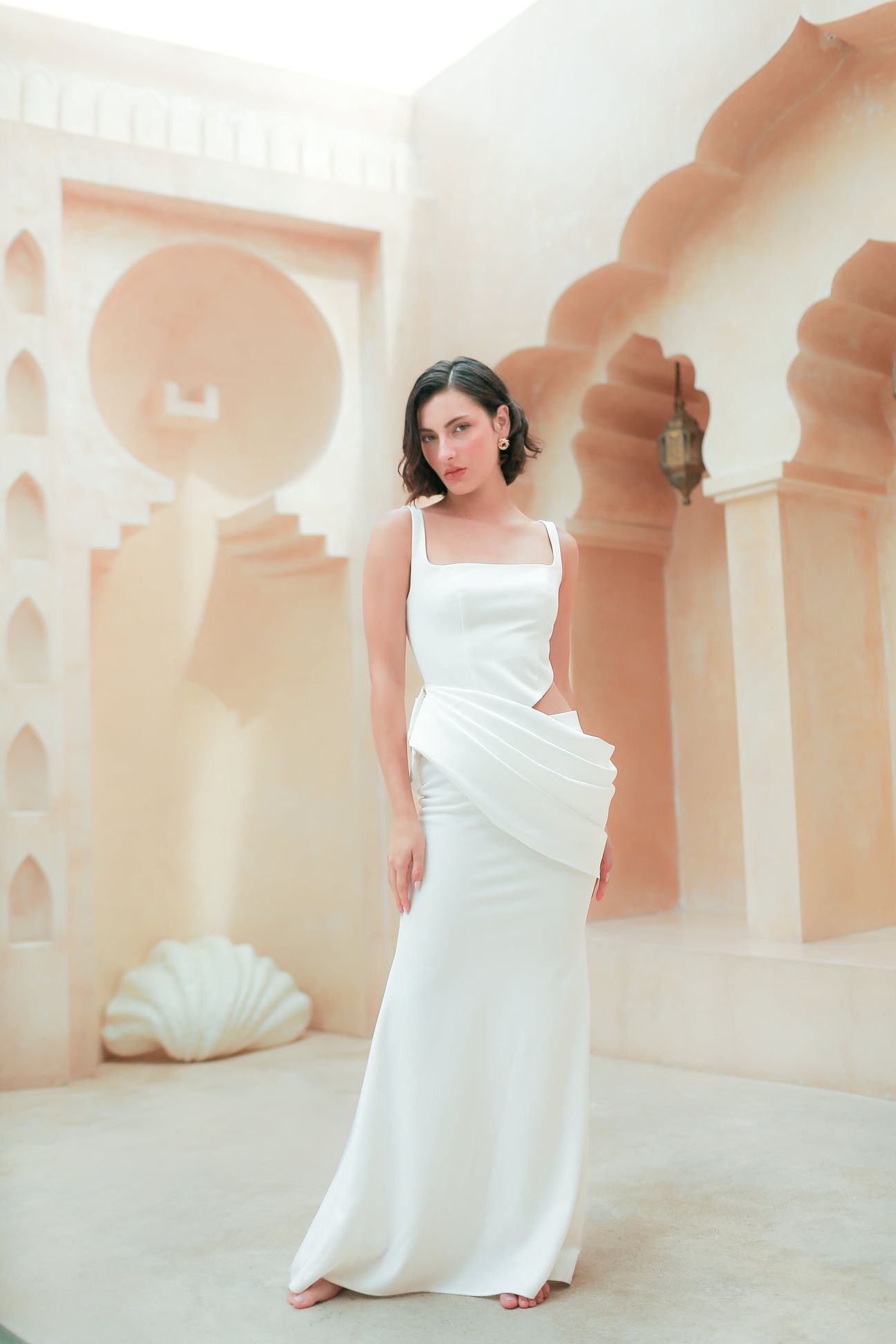 A woman in a white dress poses beside pale stone and still water